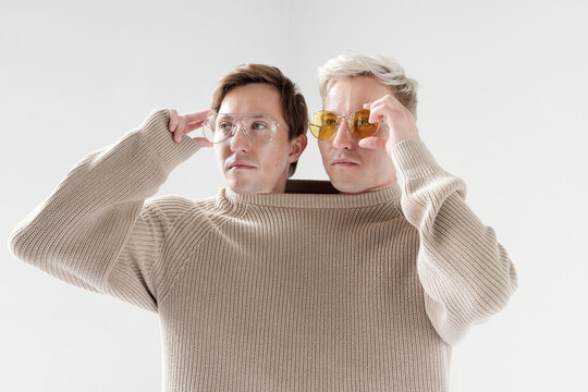 Cool Siamese brothers wearing one big sweater putting on stylish eyeglasses waist up portrait