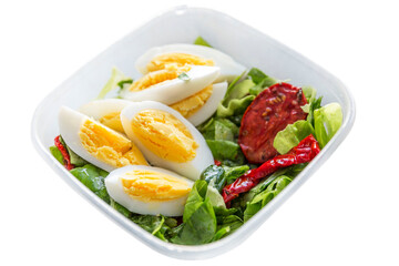 Egg halves with green salad and sun-dried tomatoes in a plastic bowl. Healthy keto diet. Isolated on white background.