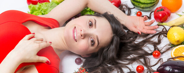 A young woman lies with ripe bright vegetables and fruits on a white background. Smiling brunette...