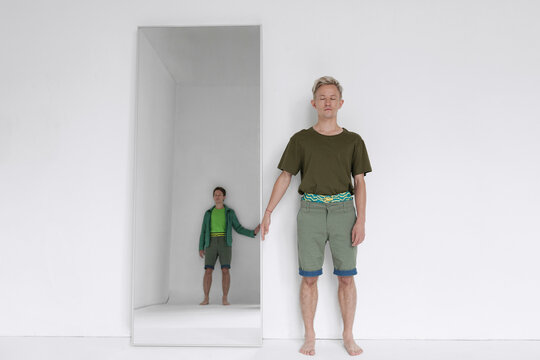 Contemporary shot of young man standing next to mirror with his twin brother reflection