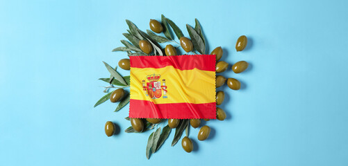 National flag of Spain and green olives with leaves on blue background