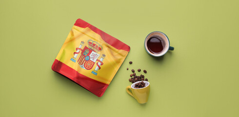 Cups with aromatic coffee and bag with print of Spanish flag on green background