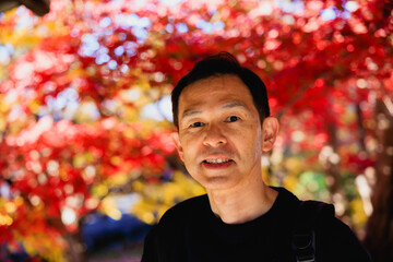 Naklejka premium Middle-aged Asian man on a sightseeing tour of the autumn leaves in Kyoto, Japan.