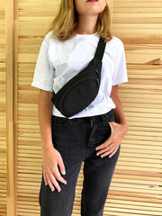 Stylish blonde girl in a white T-shirt, black jeans and a chest bag. Fanny pack woman.