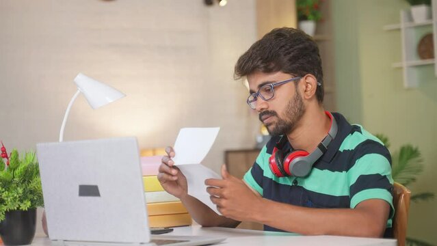 Excited young man celebrating after seeing job offer letter while sitting at home - concept of achievement, successful and knowledge.