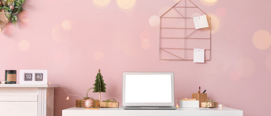 Workplace with laptop, Christmas gifts and decorations near pink wall in office