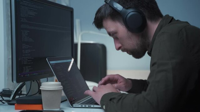 Concept of smartworking in lockdown. Man programmer in headphones sitting at at computer workplace at home office . Coding, programming. Software engineer working on programming code for new project.