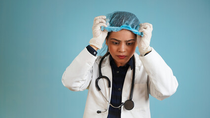 Portrait of a young female doctor wearing hand gloves, Asian Indian woman doctor in apron and stethoscope isolated over blue studio background