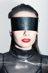 Abstract woman studio portrait with make-up and big silver futuristic eyeglasses or helmet covering her eyes. Model with red lipstick and wearing silver blouse. Tones image with blue color
