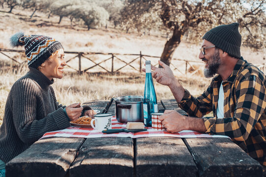 Couple of man and woman enjoying outdoor weekend leisure activity together eating on a wooden table at the park. Concept of healthy lifestyle in outdoors. Autumn season. Happy friends speak lunch - Powered by Adobe