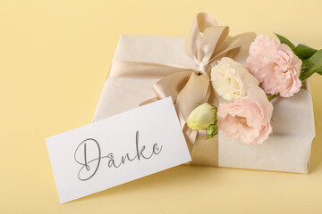 Gift box, card with text DANKE and eustoma flowers on color background, closeup