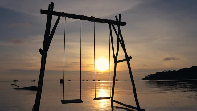 Woman at sunset on the swing at the beach, Thailand