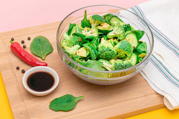Fresh Green Salad of Avocado, Broccoli, Spinach and Cucumber with Soy Sauce and Red Hot Pepper on Wooden Cutting Board. Vegan Salad. Vegetarian Culture. Raw Food. Healthy Eating and Vegetable Diet