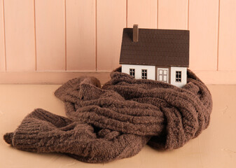 House model with scarf on beige wooden background. Heating concept