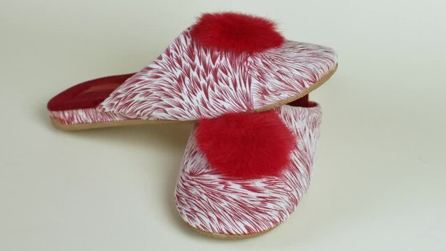 Female house slippers with beautiful motley red and white pattern with bright red pompom. Pair of female slippers for house. Modern indoor shoes for walking around house, soft, warm and comfortable