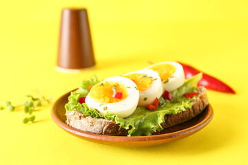 Plate of delicious toast with boiled egg on yellow background