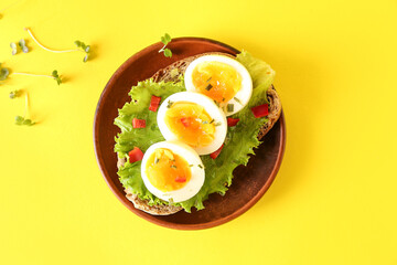 Plate of delicious toast with boiled egg on yellow background