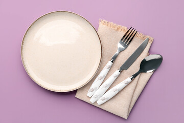 Silver cutlery with napkin and plate on lilac background