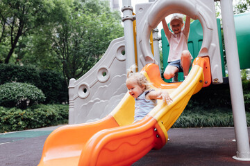 Cute blonde hair caucasian kids walking outdoor on playground at summer. Siblings having fun...