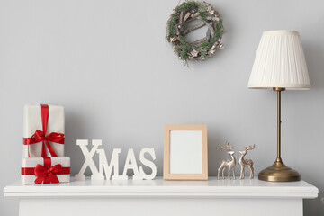 Frame with presents, lamp and Christmas decor on mantelpiece near light wall