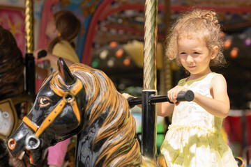 Fototapeta na wymiar Adorable little toddler girl on carousel horse. child on attraction. kid entertainment. Happy healthy baby having fun outdoor on sunny day. Family weekend, vacations, holiday