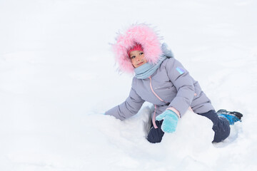 Kid playing with snowballs in fortress. Little cute ruddy girl with red cheeks throwing snow, building snowman. Christmas vacation with child in frosty winter Park. Wintertime, active game outdoor