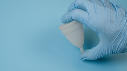 A hand in a medical, latex glove holds a hygienic, menstrual cup. Women's health concept.