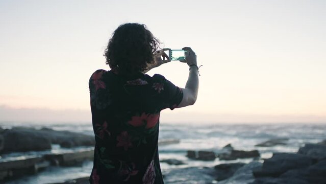 Beach, sunset and photography, man with phone taking holiday picture in Bali. Vacation, technology and travel, photographer capturing zen view of sea, sun and sky on smartphone camera in Indonesia.