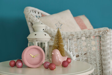 Alarm clock with Christmas decor and lantern on table near blue wall