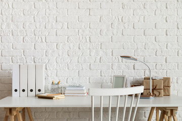 Workplace with frame, books, lamp and Christmas presents near white brick wall