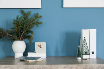 Vase with Christmas branches, clock and folders on table near blue wall