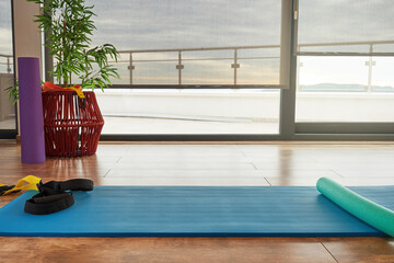 Sunlit fitness center with exercise mat and sport equipment. Wide open windows and the blue sky