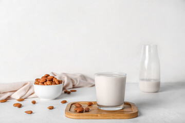 Board with glass of almond milk and nuts on white table