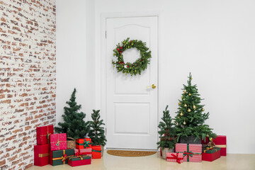 White door with Christmas wreath, fir trees and presents in hall