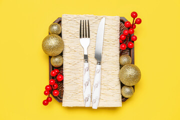Table setting with Christmas balls and cranberry on yellow background