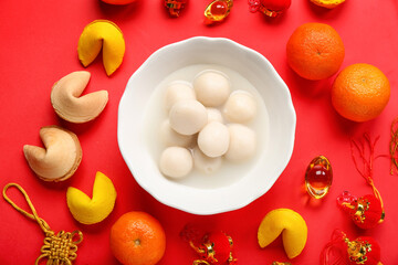 Bowl of tasty tangyuan, fortune cookies, mandarins and Chinese decor on red background. Dongzhi...