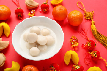 Bowl of tasty tangyuan, fortune cookies, mandarins and Chinese decor on red background. Dongzhi Festival