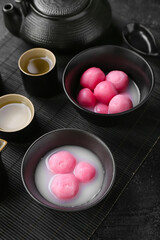Bowls of tangyuan, cups and teapot on black bamboo mat. Dongzhi Festival