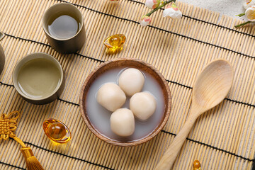 Bowl of tangyuan, cups and Chinese decor on bamboo mat. Dongzhi Festival