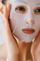 Young woman applies white sheet mask to her face