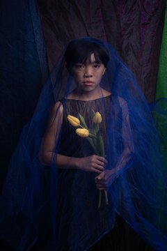 fine art studio portrait of asian boy holding tulip flowers covered by thin veil and fabric