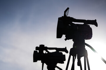 Silhouette of two television broadcasting cameras against a sunny day. TV and journalism.