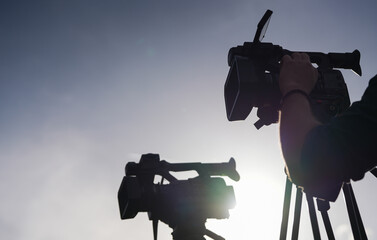 Silhouette of two television broadcasting cameras with the hand of a cameraman operator controlling...