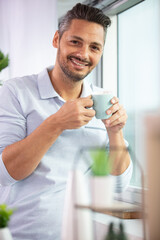 man holding a coffee cup beside a window