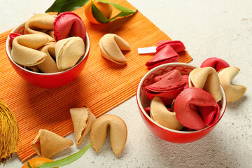 Bamboo mat with bowls of fortune cookies and mandarins on light background, closeup