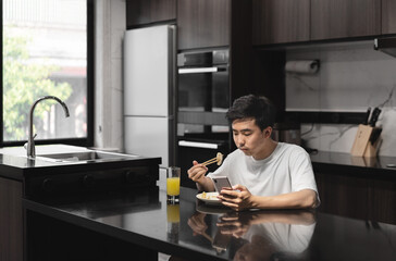 Asian man is eating breakfast while using mobile phone.