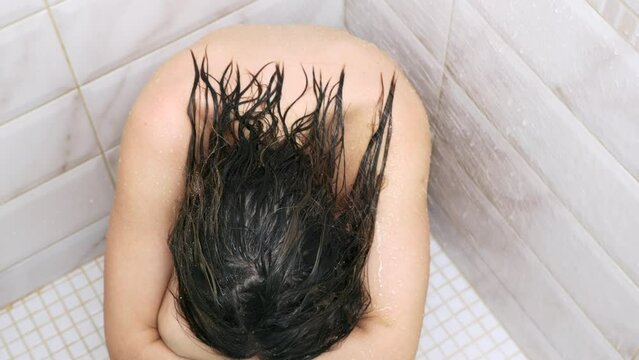 Girl with wet hair in depression squats in the corner of the shower under jets of warm water. An upset young woman sat down in the shower under warm water, crying and sad