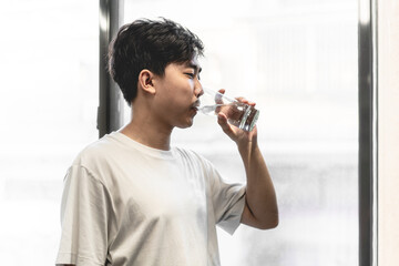 Fototapeta na wymiar Asian young man is drinking water near the window.