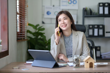 Asian businesswoman, real estate agent, talking on the phone with a customer about the details of...