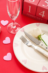 Cube calendar with date 14 FEBRUARY, table setting and hearts on red background, closeup